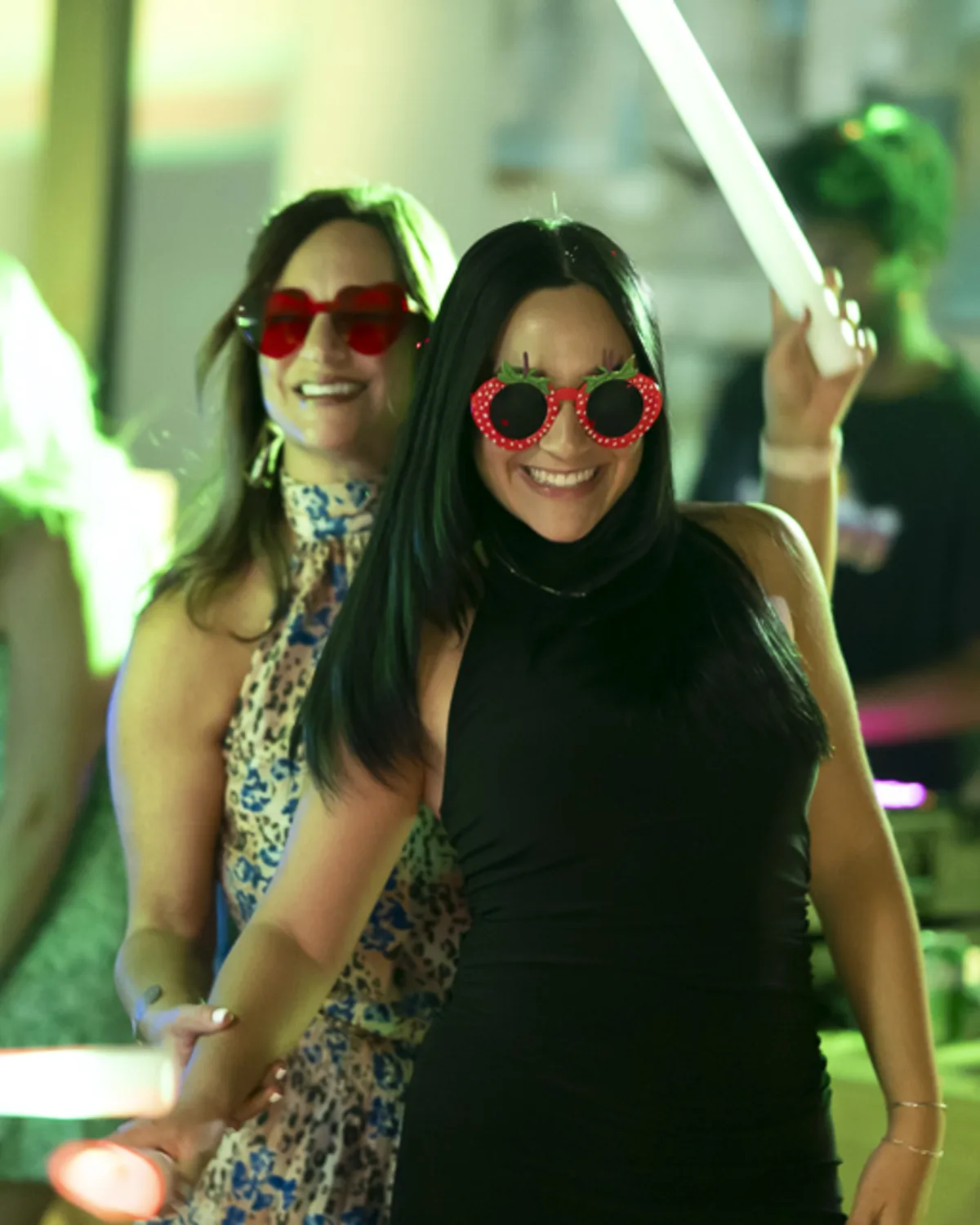 Two women in heart-shaped glasses dancing with glow sticks at a lively
party in Denver, captured with vibrant event photography