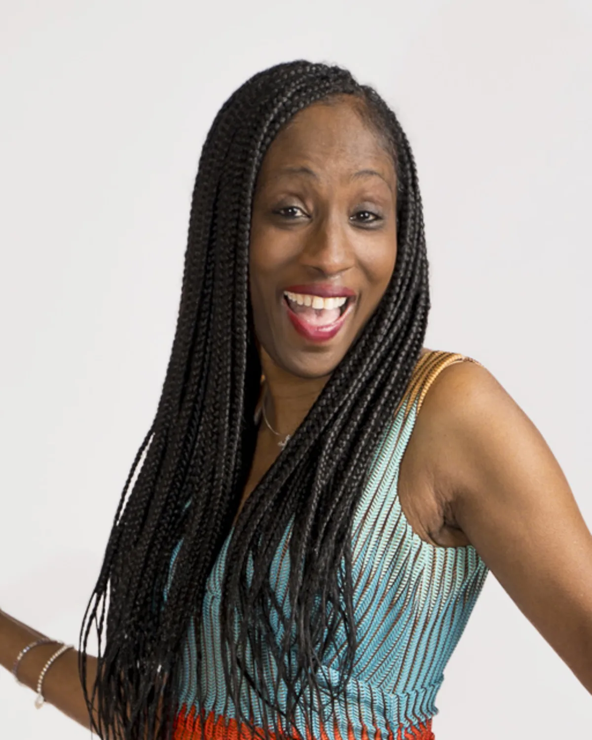 Black woman with long braids smiling joyfully, striking a playful pose in
a studio setting
