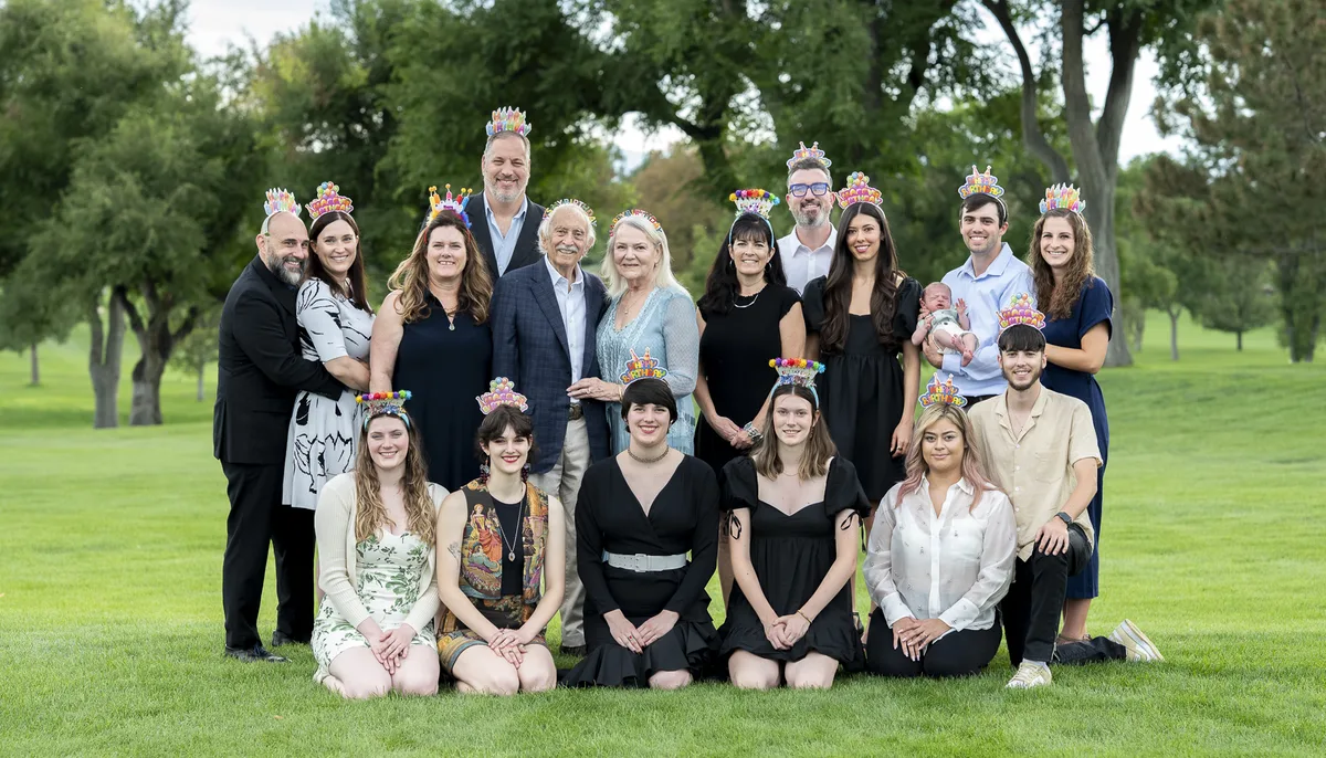 Large multigenerational and LGBTQ-inclusive family posing together in a park
during playful outdoor portrait session in Denver, all wearing birthday crowns