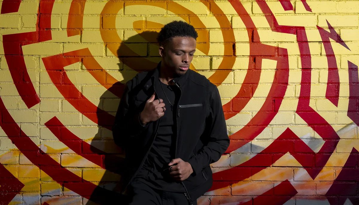 Black high school senior posing confidently in black outfit against bold
street art mural during urban senior portrait session in Denver