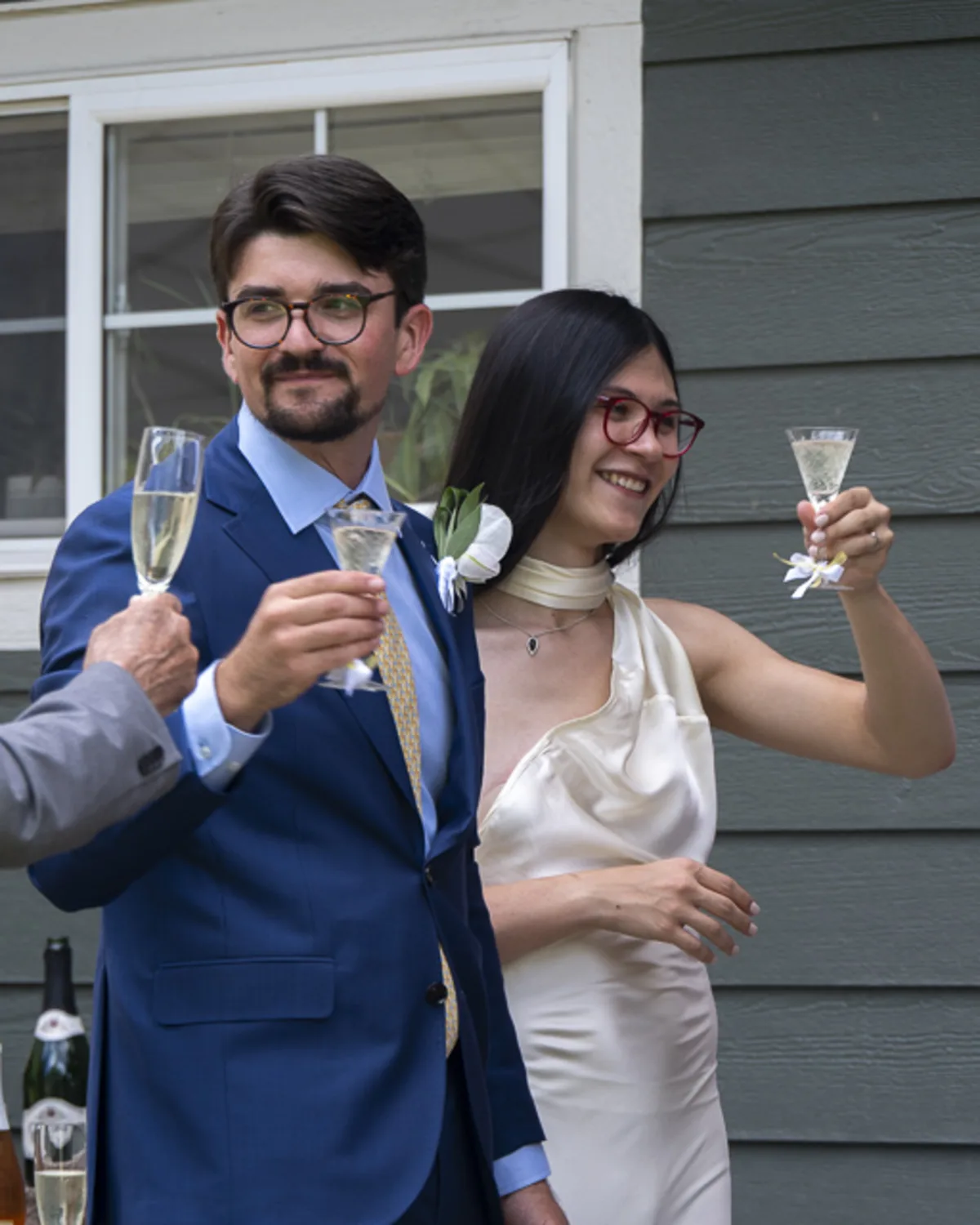 Trans bride and her partner raise champagne glasses during a joyful
backyard wedding celebration with friends
