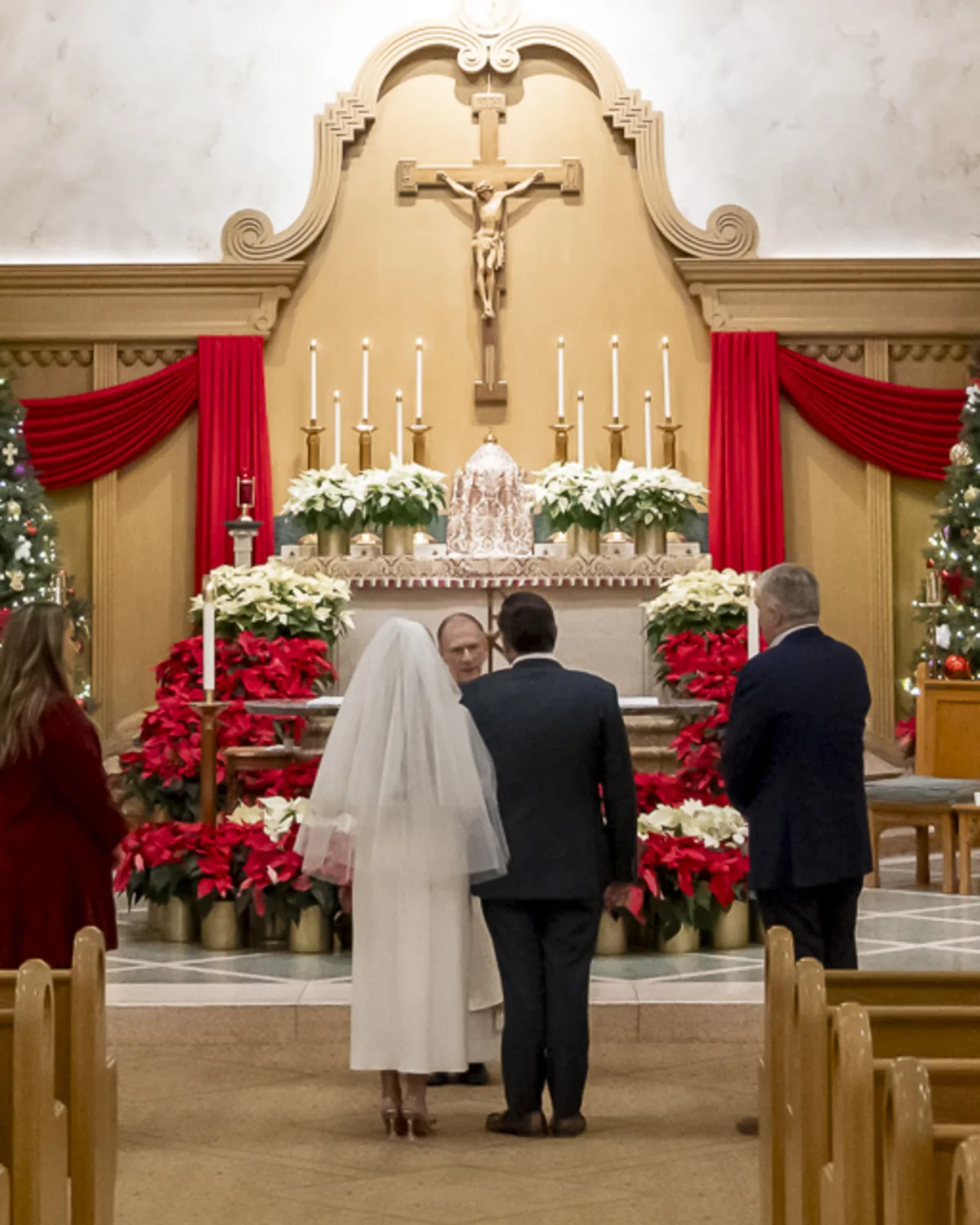 Bride and groom stand before a priest at the altar of a Catholic church
decorated for Christmas, preparing to exchange vows.