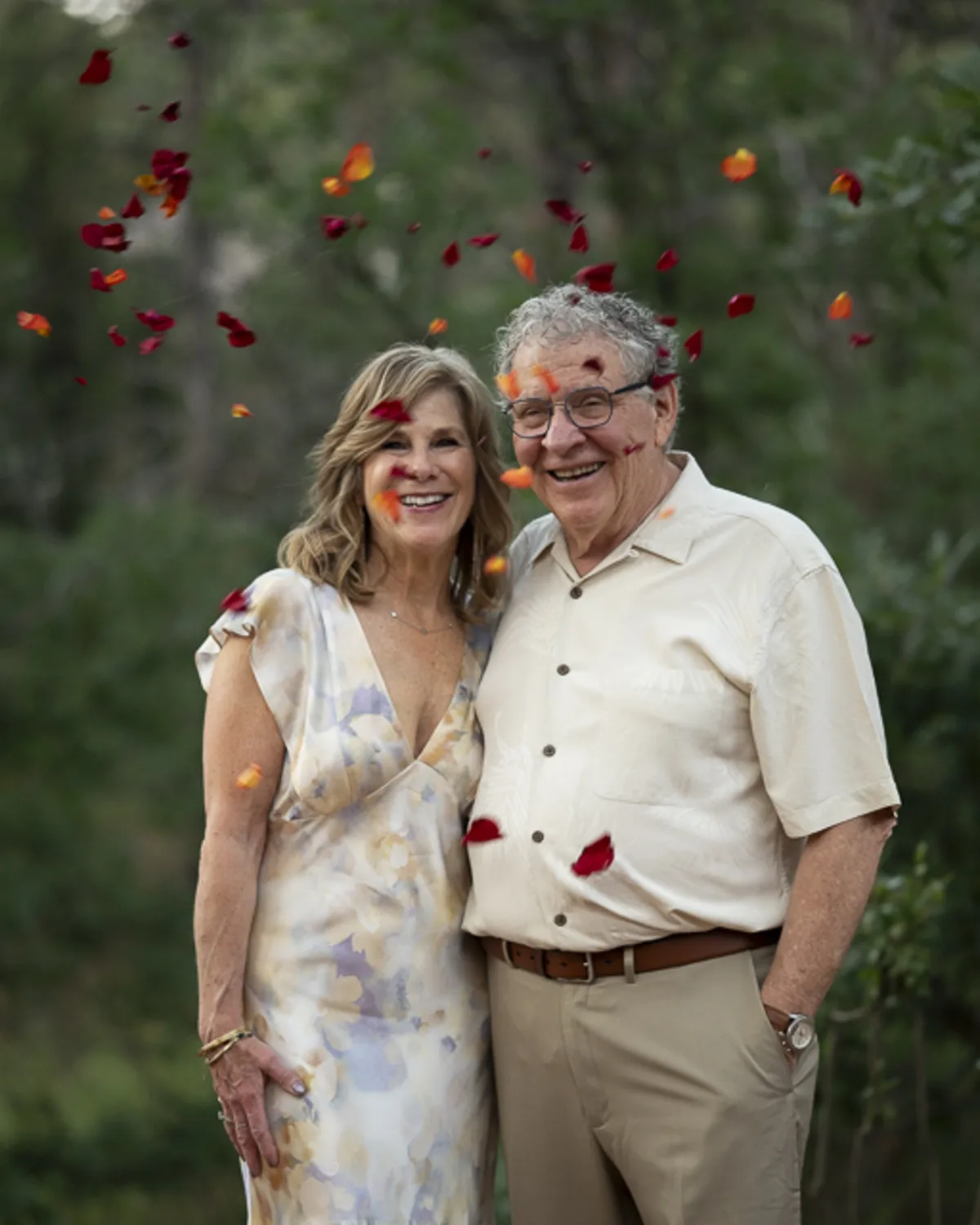 An older Jewish couple smiling together outdoors during a wedding
celebration, surrounded by falling flower petals